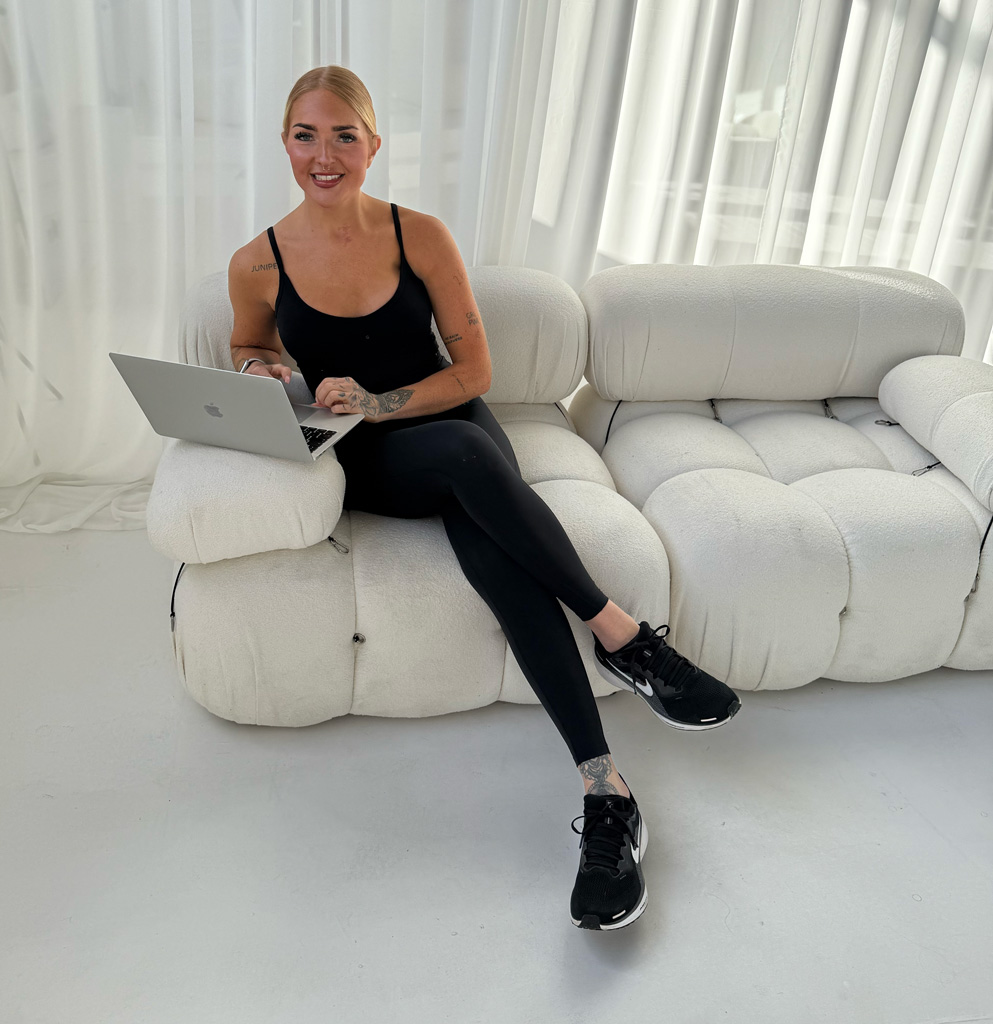 The coach is sitting on couch while working on her laptop.